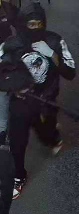 A person in dark-colored clothes and gloves with their face covered at the scene of the crime.