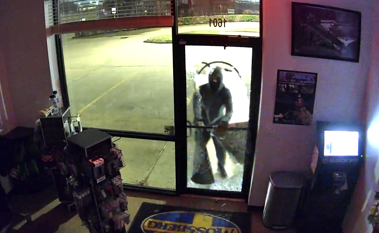 A person in a hoodie and a face-covering at the door of a store.
