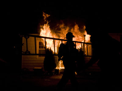 Certified fire investigator with a ladder in front of a house on fire