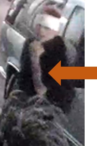 Person of interest wearing a dark top, white cloth wrapped are their head, carrying a bag, leaning against a vehicle. Person of interest wearing a dark top, white cloth wrapped are their head, carrying a bag, leaning against a vehicle.