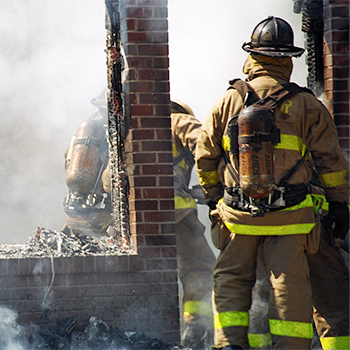 Individuals in protective gear approach a smoke-filled building