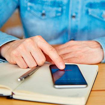 An individual uses their phone next to a notebook and pen