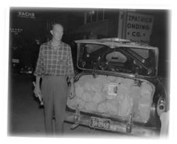 Image of an agent standing behind a car with the trunk open displaying bags of sugar.