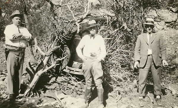 Image of three searchers posing in front of Sutton's sedan hidden under brush.