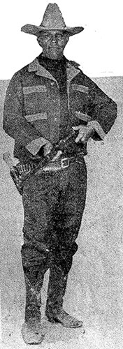 Full Image of Tom Threepersons holding a rifle and carrying a holstered pistol.