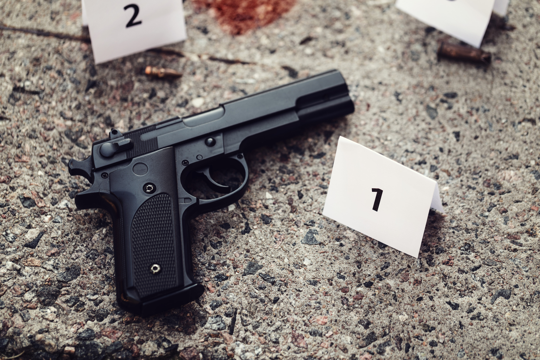 Handgun lying on bloodstained floor next to evidence markers.