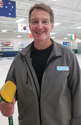 Ed holding a curling broom, standing on an ice rink.