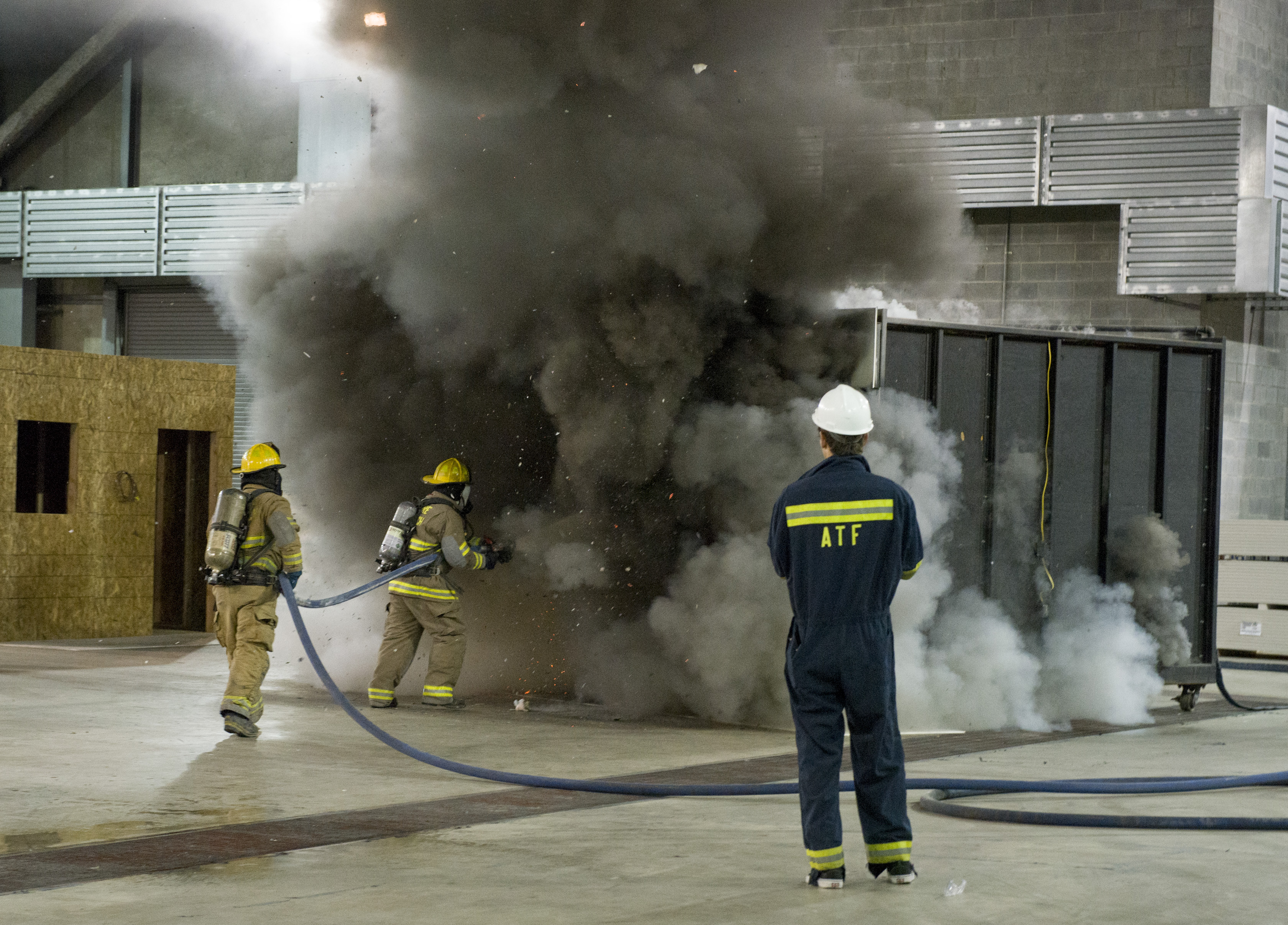 Two firemen use their hoses to extinguish a fire overseen by an ATF instructor.