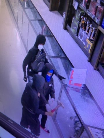 Three suspects breaking glass on a display with a hammer.