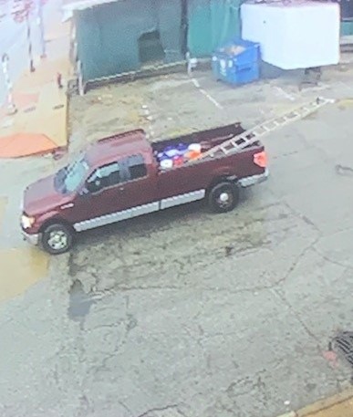 The side of a dark-colored truck with a ladder and other materials in the back of it.