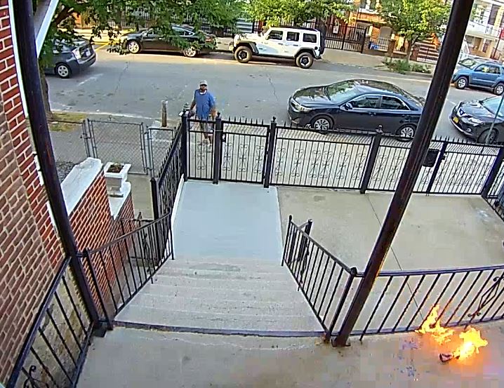 A person looking up at a Molotov cocktail that was thrown onto the porch of a house.