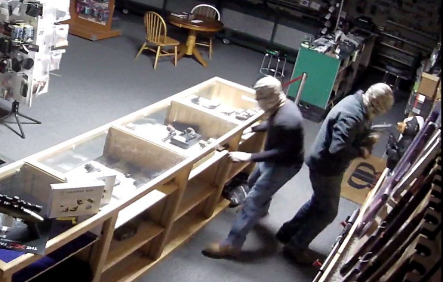 Two suspects in full face masks looking at items and burglarizing a gun shop.