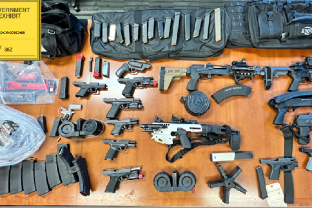 Large amount of guns and ammunition, arranged on a table, collected as evidence by law enforcement agents.