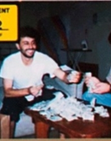 Two men sitting in front of a table with a pile of cash on top