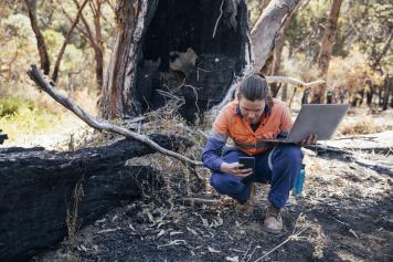 Woman takes pictures of possible evidence on the ground with a laptop in her other hand