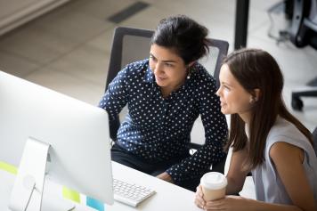Two females collaborating in front of a laptop while at work