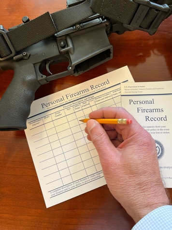 A person writes on an ATF Personal Firearms Record next to a firearm
