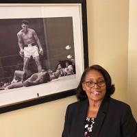 Carla Young Senior Attorney stands in front of a poster of boxer Muhammad Ali