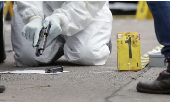 A forensics specialist recovers a firearm and bullets from a crime scene