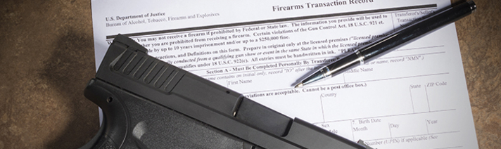 A firearm and a pen on top of an official application to own or manufacture a firearm