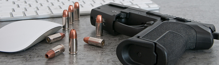 Gun and bullets on a desk next to a computer