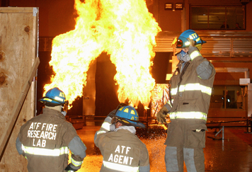 Individuals in ATF fire gear in front of a fire