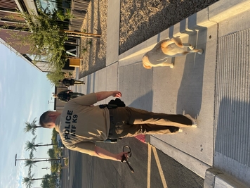 A special agent canine handler and their canine walk with palm trees in the distance